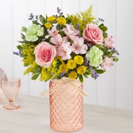 Pink roses and mixed flowers arranged in a peach glass vase