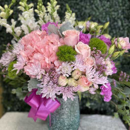 Pink and lavender bouquet in a textured vase with a magenta ribbon