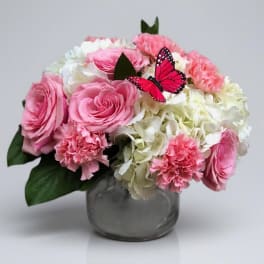 Pink and white flower arrangement in a glass vase with a butterfly accent