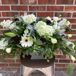 White floral arrangement in a gray vase with mixed greenery