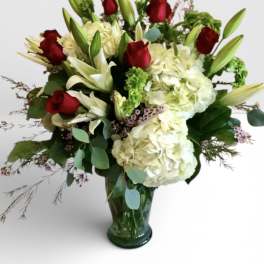 Red roses and white lilies with hydrangeas in a green glass vase