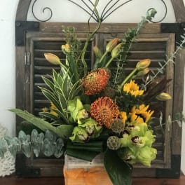 Tropical floral arrangement in a wooden box with orange and green blooms
