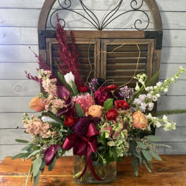 Mixed floral arrangement in a glass vase with burgundy ribbon