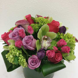 Pink and lavender roses with green orchids in a round vase