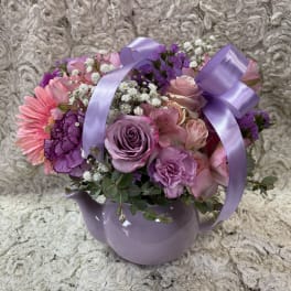 Pink and purple flower arrangement in a lavender teapot vase with ribbon