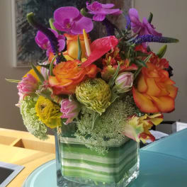 Colorful bouquet in a square glass vase with orchids and roses