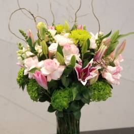 Pink and white floral arrangement in a glass vase with tall curly branches