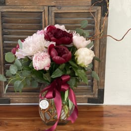 Bouquet of pink and burgundy peonies in a glass vase with a ribbon