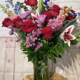 Bouquet of red roses, pink lilies, and purple flowers in a glass vase