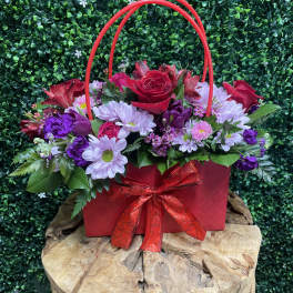 Red and purple flower arrangement in a red gift bag with ribbon