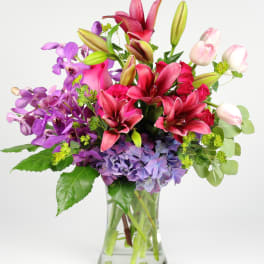 Mixed bouquet of pink lilies, purple orchids, and lavender hydrangeas in a glass vase