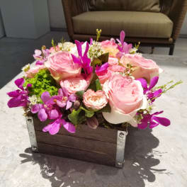 Pink roses and purple orchids arranged in a wooden box