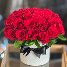 Red roses arranged in a white hatbox with a black ribbon