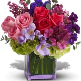 Bouquet of pink and red roses with purple flowers in a square vase