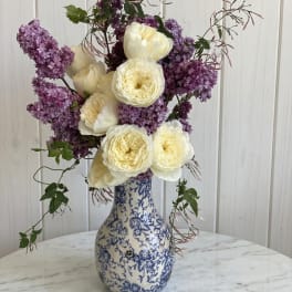 White roses and purple lilacs in a blue-and-white vase
