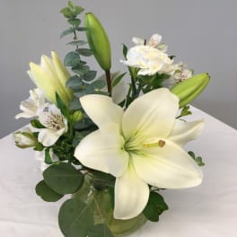 White lilies and alstroemeria arranged in a glass vase.