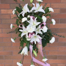 Standing white lily and carnation spray with pink ribbon on an easel