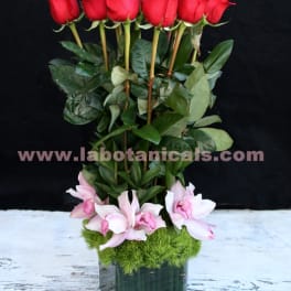 Tall arrangement of red roses and pink orchids in a square glass vase