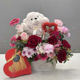 Teddy bear in a heart-shaped floral arrangement with red and pink flowers