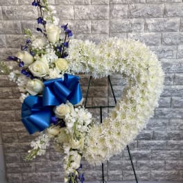 White floral heart wreath with blue ribbon on a stand
