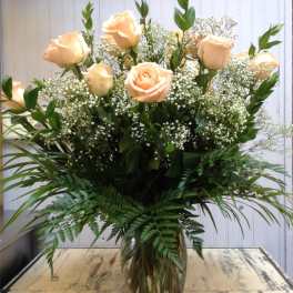 Peach roses in a clear glass vase with baby's breath and greenery