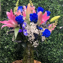Bouquet of pink lilies, blue roses, and white baby's breath in a glass vase