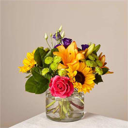Mixed bouquet of sunflowers, roses, and lilies in a glass vase