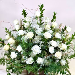 Large white rose arrangement in a wicker basket with greenery