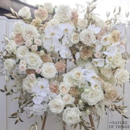 Large white floral arrangement with roses and orchids on an easel