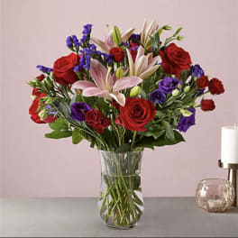 Bouquet of red roses, pink lilies, and purple flowers in a glass vase