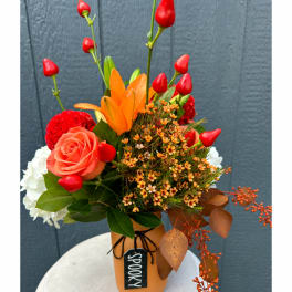 Bright mixed bouquet in a tan vase with red buds and orange lilies
