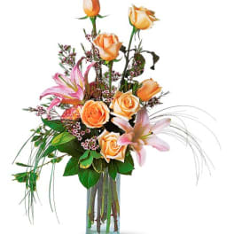 Tall bouquet of peach roses and pink lilies in a glass vase