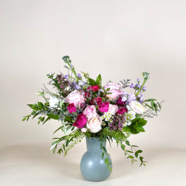 Pink and lavender roses, carnations, and daisies arranged in a matte blue vase.