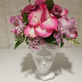 Pink and white rose arrangement in a clear glass vase shaped like a face