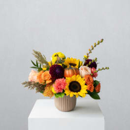 Mixed bouquet with sunflowers, roses, and a small pumpkin in a ribbed vase