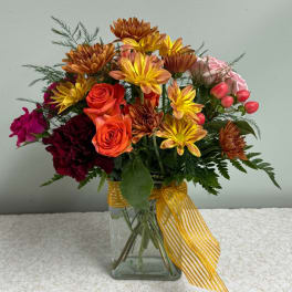 Mixed bouquet of roses and chrysanthemums in a glass vase with a yellow ribbon