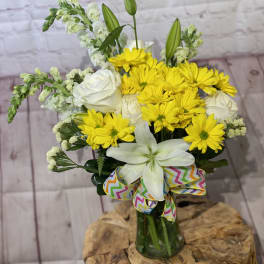 Yellow daisies and white lilies in a glass vase with a colorful ribbon