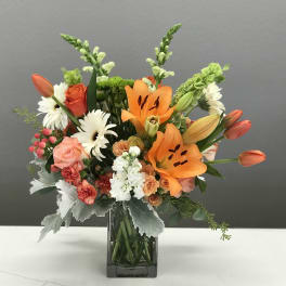 Mixed bouquet with orange lilies, roses, and white daisies in a glass vase