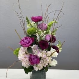 Pink and purple flowers arranged in a square glass vase with curly branches