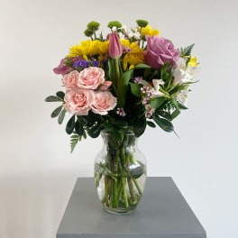Mixed bouquet of pink roses, yellow daisies, and white flowers in a glass vase