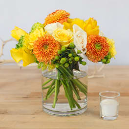 Yellow and white bouquet in a clear glass vase with a small candle nearby
