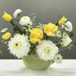 Yellow tulips and white flowers arranged in a green vase