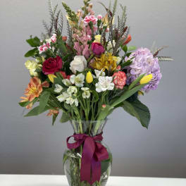 Mixed bouquet in a clear glass vase with a magenta ribbon