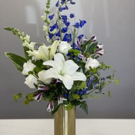 White lilies and blue flowers arranged in a gold vase
