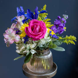 Mixed bouquet with a pink rose, purple iris, and yellow filler in a glass vase