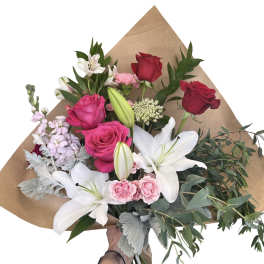 Bouquet of red and pink roses with white lilies and greenery in brown paper
