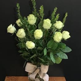 White roses arranged in a clear glass vase with a beige ribbon