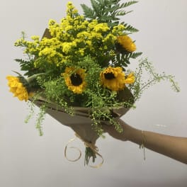 Bouquet of yellow sunflowers and small yellow filler flowers wrapped in brown paper
