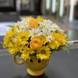 Yellow and white flowers arranged in a smiley-face mug
