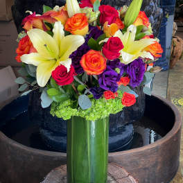 Bouquet of lilies, roses, and purple blooms in a tall green vase